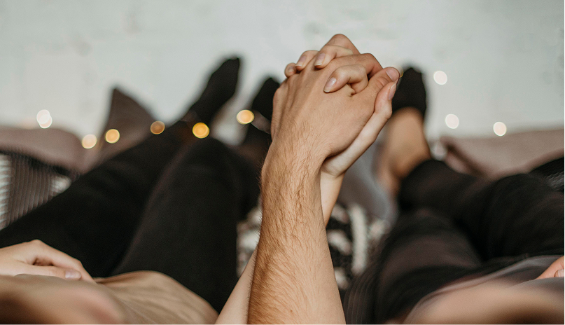 Primer plano de una pareja tomados de la mano en la cama, en un contexto de terapia sexual.